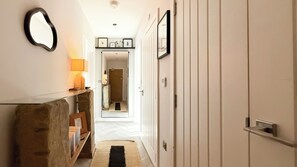 Un couloir avec un miroir, une lampe, un banc en bois et une porte donnant sur une autre pièce.