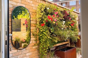 Un muro de ladrillo con un espejo y un jardín vertical con diversas plantas y flores.