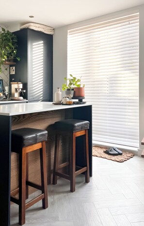 Une cuisine moderne avec un îlot central, des tabourets de bar, une machine à café et une plante en pot.