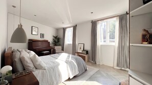 Un dormitorio con cama, piano, escritorio, lámpara y ventana con cortinas.