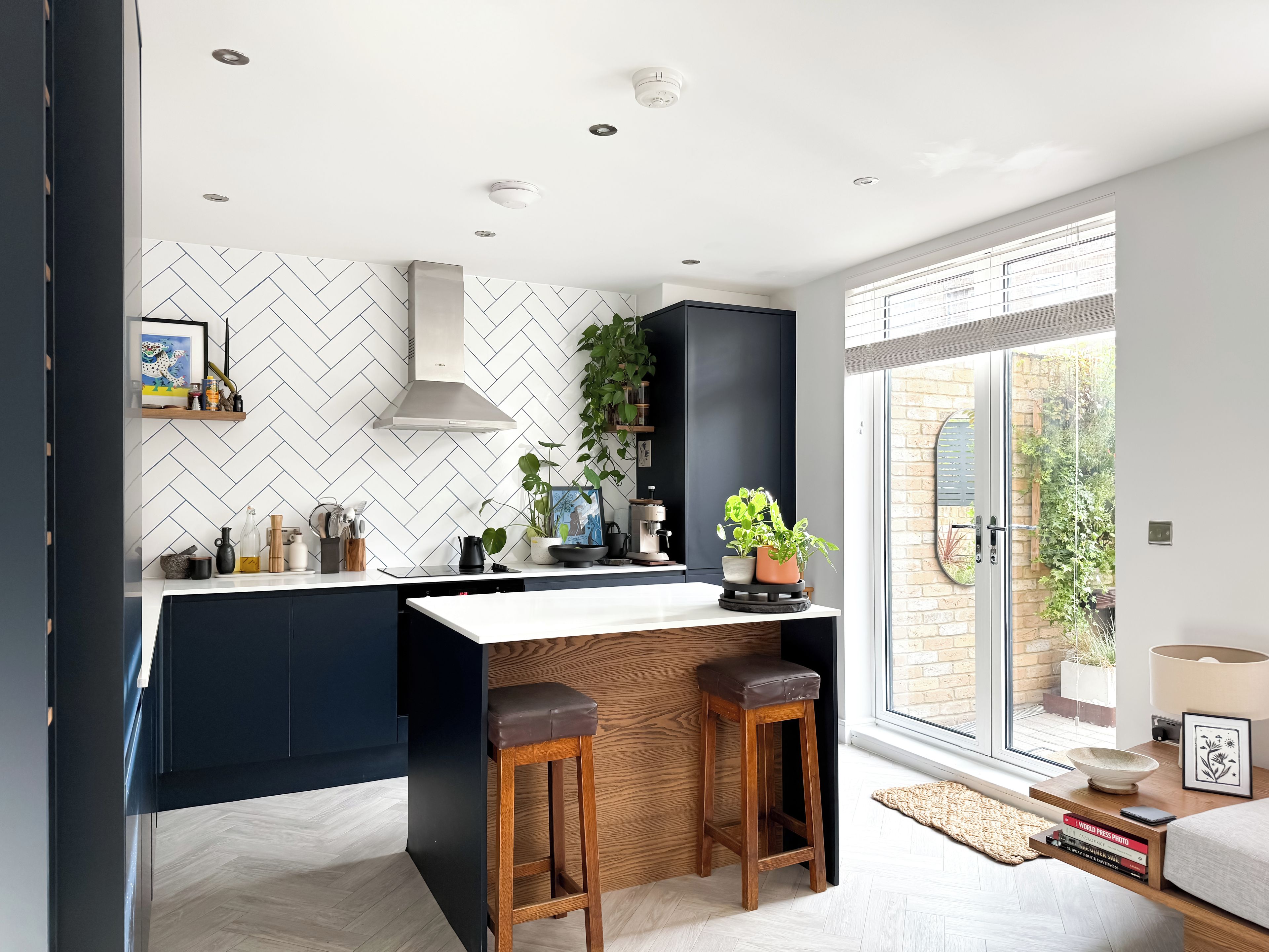 Une cuisine moderne dotée d’un îlot central, de meubles de rangement aux couleurs sombres et d’un dosseret en carreaux disposés en motif chevrons.