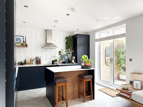 A modern kitchen with a central island, dark cabinetry, and a herringbone tile backsplash.
