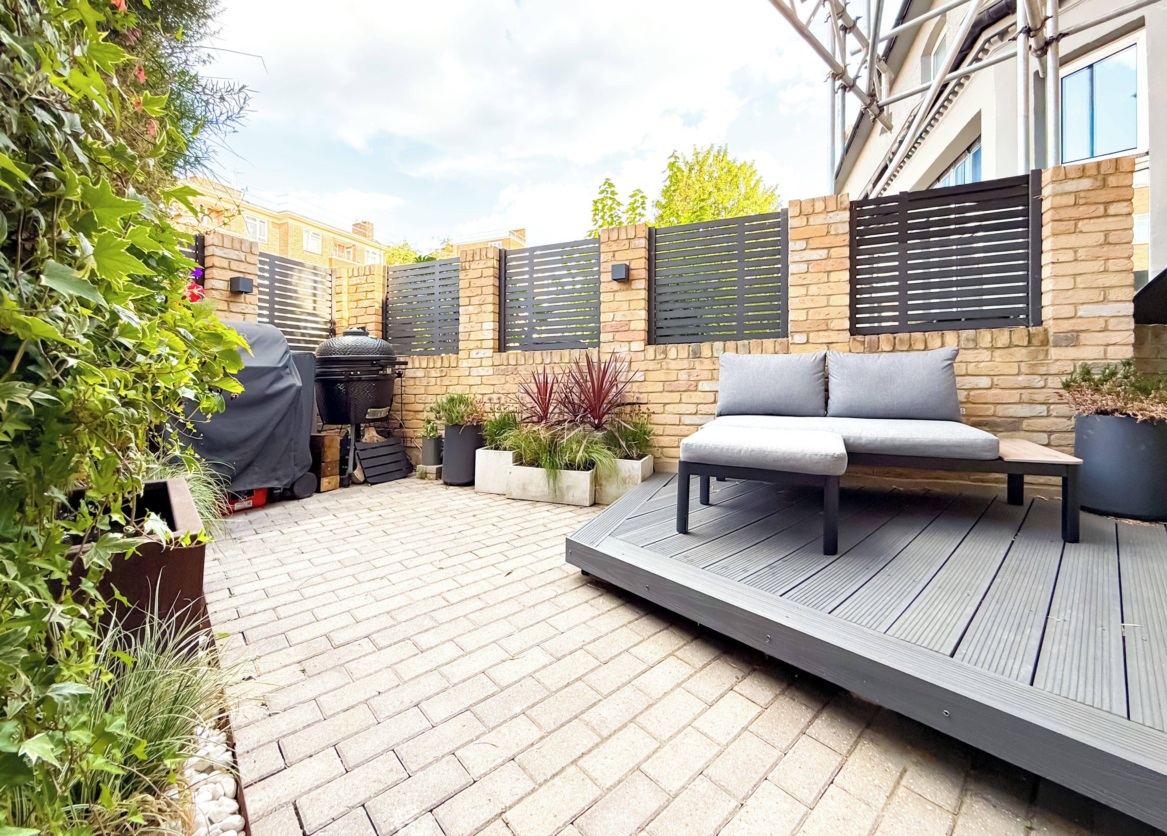 A patio with a built-in bench, a barbecue grill, and potted plants.