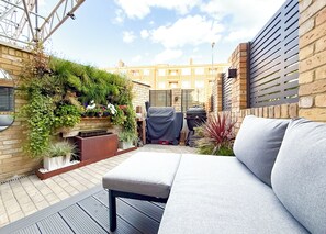 Una terraza en la azotea con un sofá gris, una parrilla y diversas plantas.