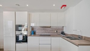 Una cocina moderna con muebles blancos, horno empotrado, cafetera y lavabo.