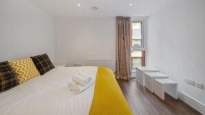 Habitación de hotel con una cama grande, una ventana con cortinas, un radiador y una mesita blanca.