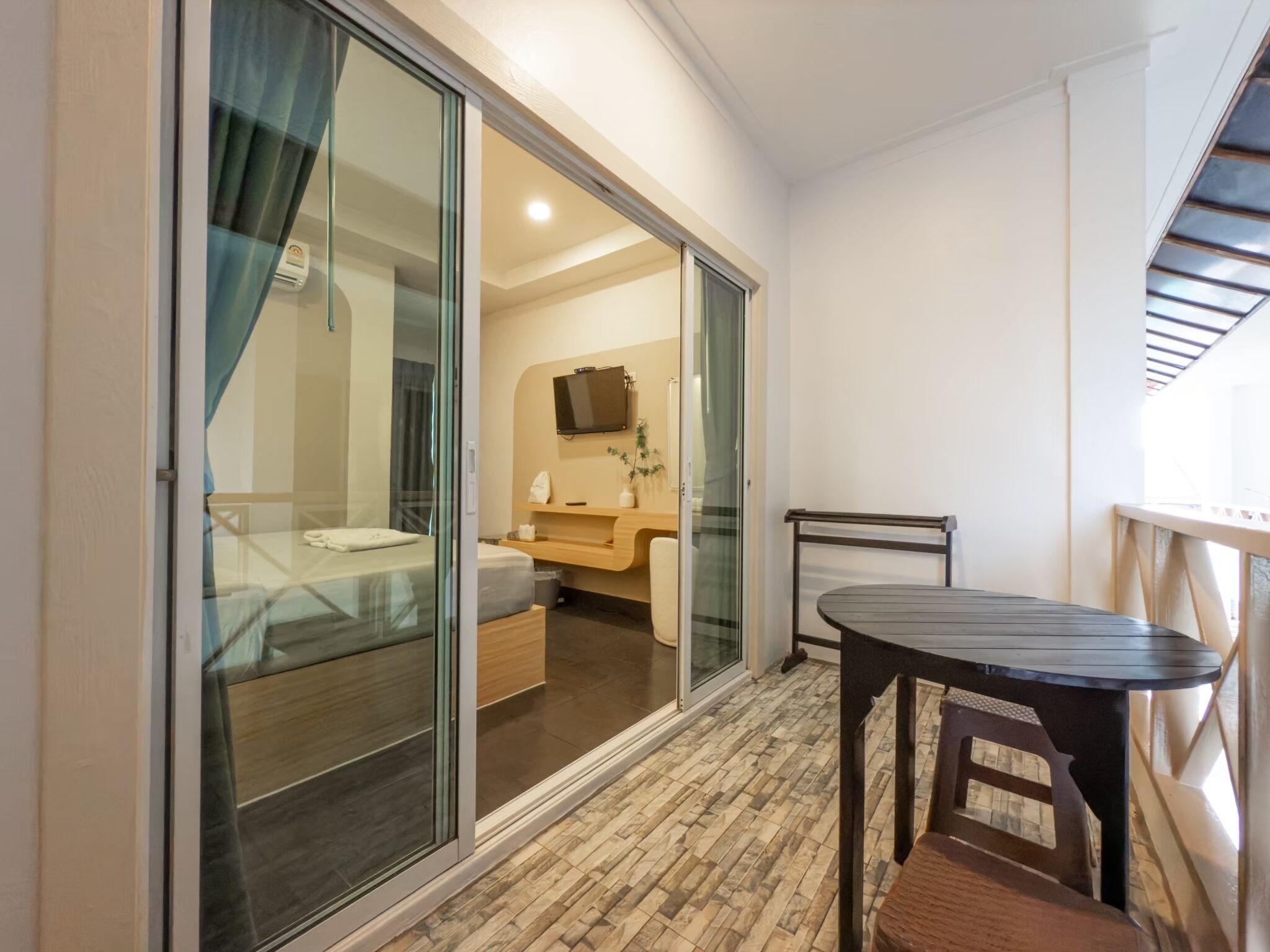 Una habitación de hotel moderna con una puerta corredera de vidrio que da a un balcón, una mesita pequeña y una cama con cabecera de madera.