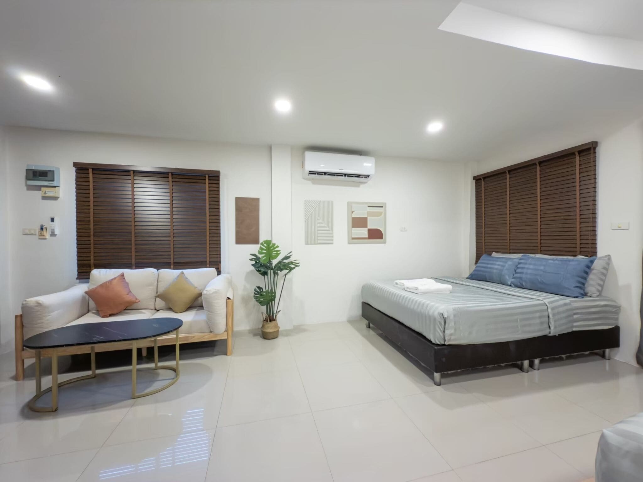 A modern bedroom with a bed, a sofa, a small table, and a potted plant.