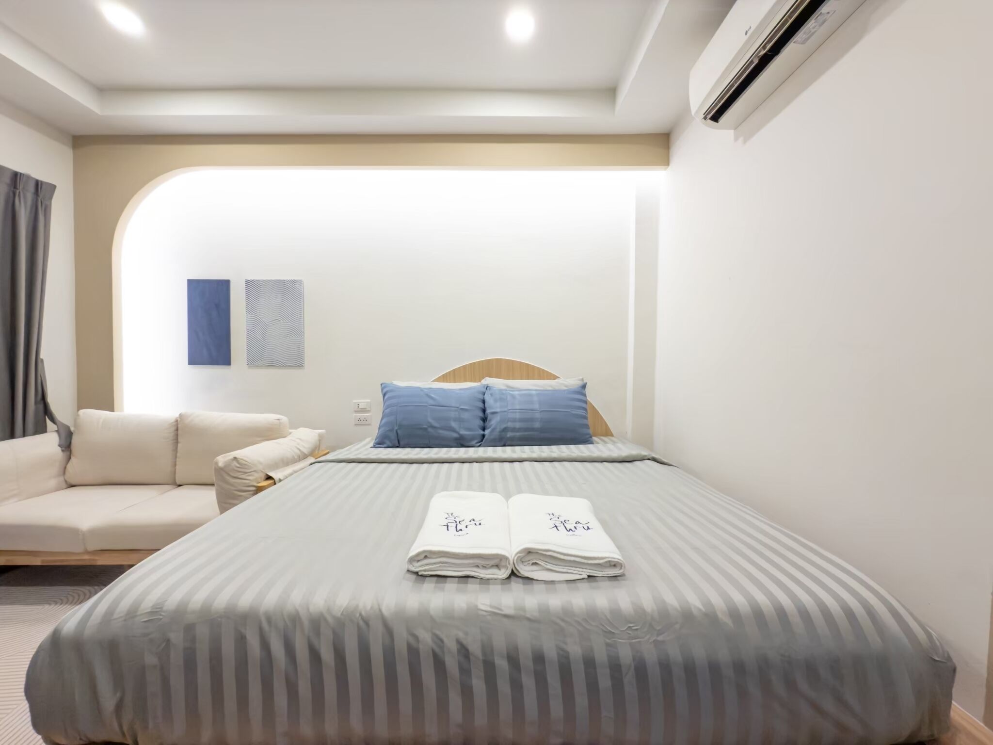 Una habitación de hotel moderna con una cama bien hecha, un sofá y un aire acondicionado instalado en la pared.