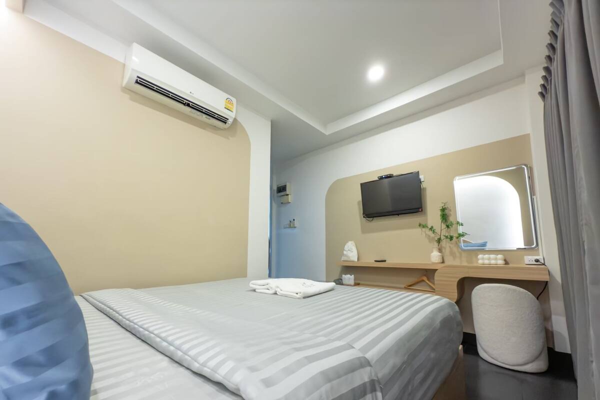 A hotel room with a bed, a desk with a chair, a TV, and an air conditioning unit.