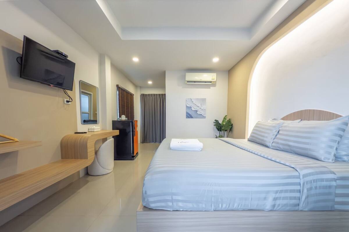 A modern hotel room with a large bed, a desk, a flat-screen TV, and an air conditioning unit.