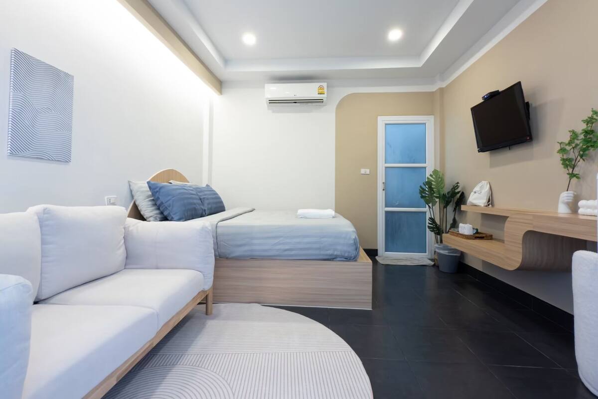 A modern hotel room with a sofa, a bed, a flat-screen TV, and a reception desk.