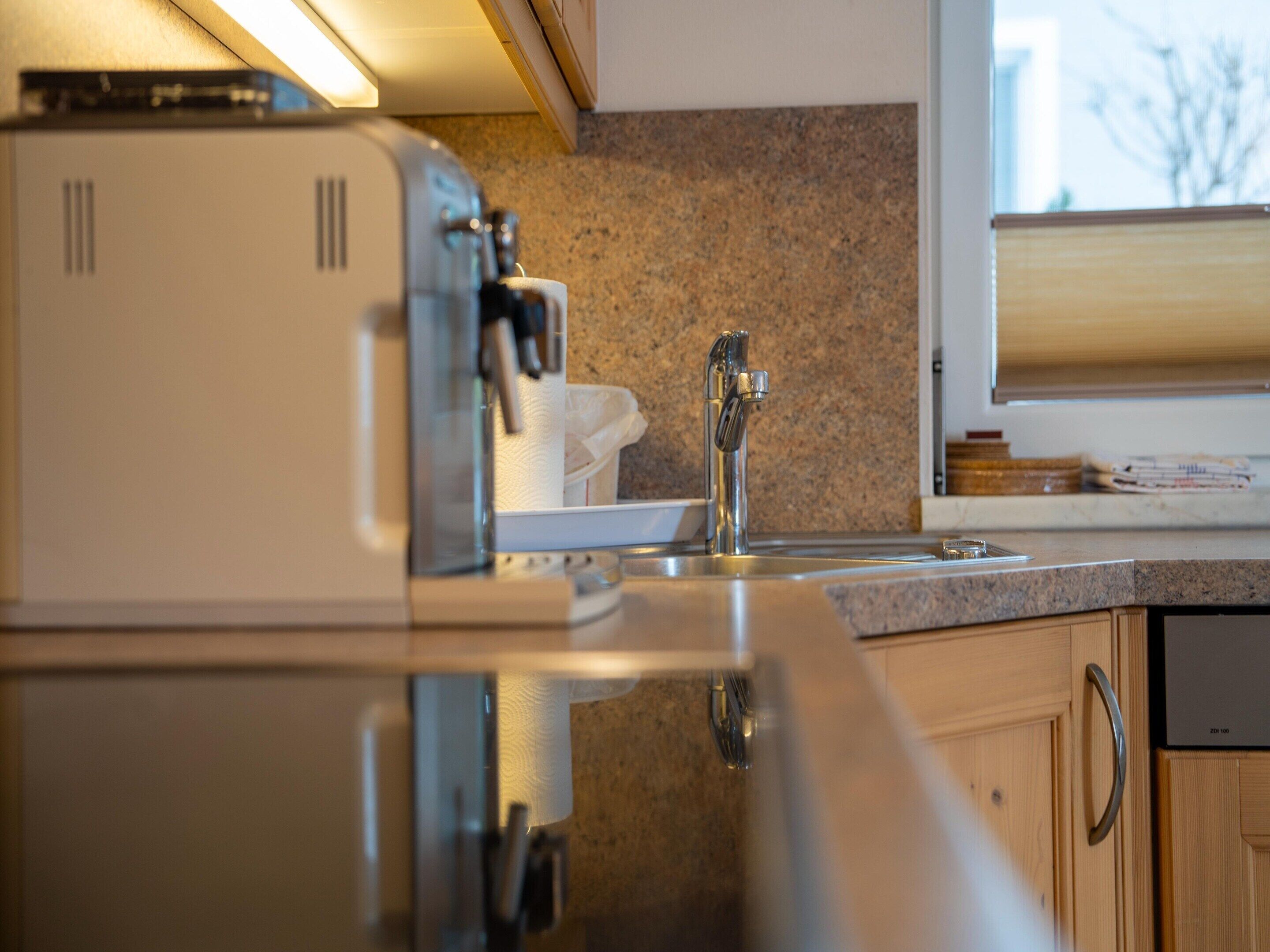 A kitchen with a stainless steel range hood, a granite countertop, a stainless steel sink, and wooden cabinets.