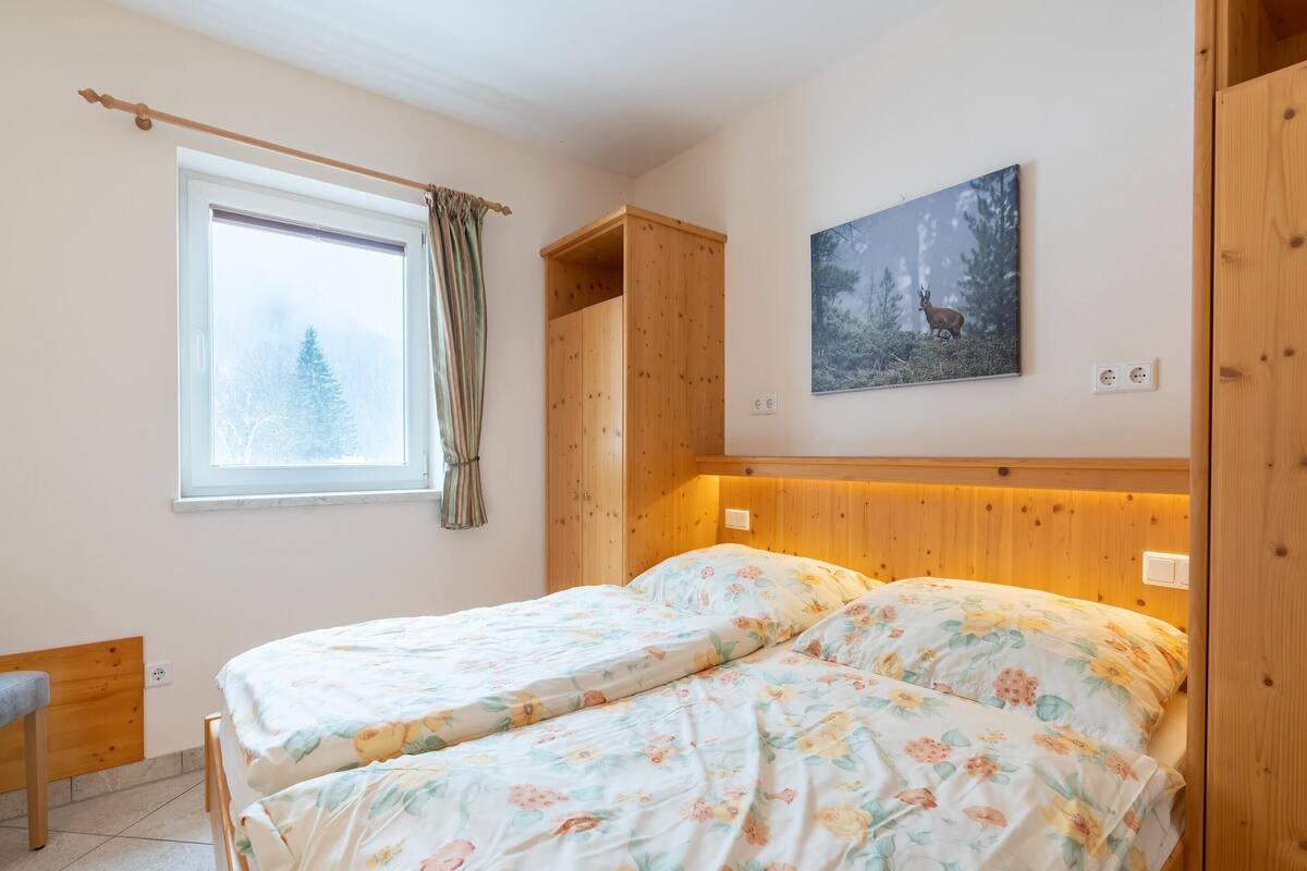 A bedroom with two beds, a wooden wardrobe, a window with curtains, and a painting of a deer.