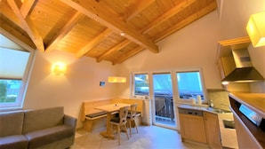 A cozy kitchen with wooden beams, a dining area with a bench, and a sofa.