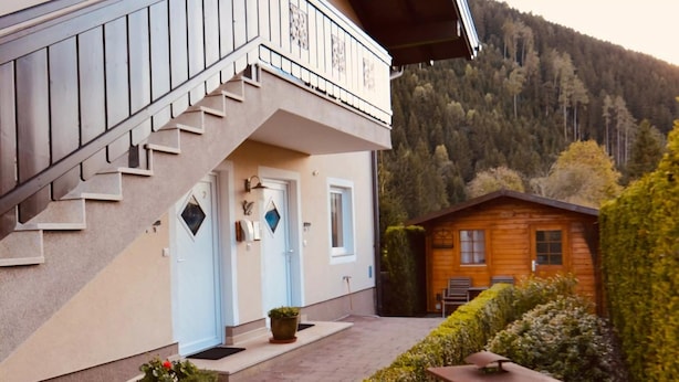 A two-story building with a balcony, a wooden cabin, and a mountainous backdrop.
