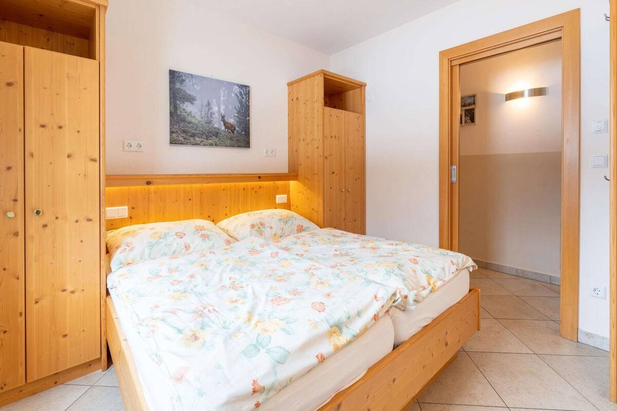 A bedroom with a wooden bed, a nightstand, a wooden wardrobe, and a door with a light switch.