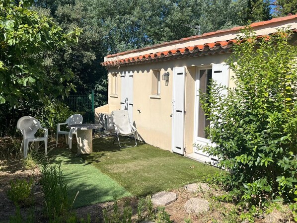 A small building with a tiled roof, a door, and a window. There is a table and two chairs outside.