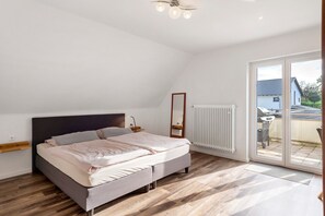Un dormitorio con cama, una mesita de noche, un espejo, un radiador y un ventanal corredizo al exterior.