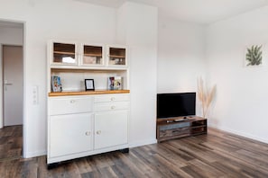 Una habitación con un armario blanco, un televisor de pantalla plana y suelo de madera.
