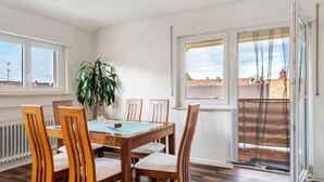 Een eetgedeelte met een houten tafel en stoelen, een potplant en uitzicht door een schuifdeur.