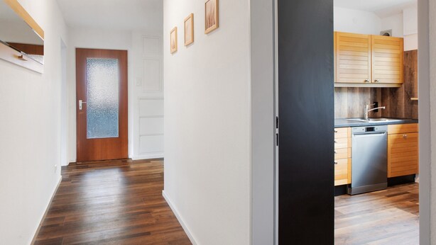 Een hal met houten vloeren, een deur met geëtste glas en een keuken met houten kastjes en een vaatwasser.