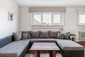 Una sala de estar moderna con un sofá modular, una mesa de centro de madera y un ventanal con vistas a edificios.