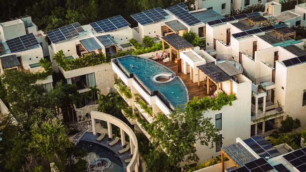 Ett bostadskomplex med flera byggnader, solpaneler, en swimmingpool och en cirkelformad vattendekoration.