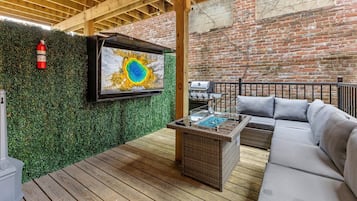 Een houten terras met een televisie, buitenbank en barbecueplaats.