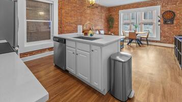 A kitchen with a large island, white cabinets, and a stainless steel trash can.