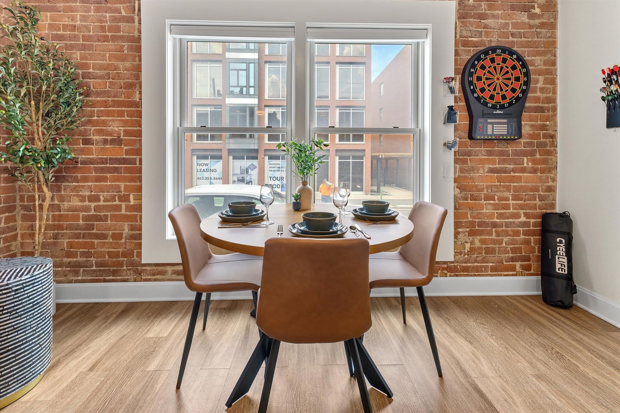 A dining area with a brick wall, a dartboard, and a view of buildings outside.
