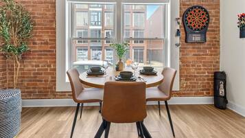 A dining area with a brick wall, a dartboard, and a view of buildings outside.