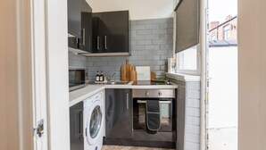 Una cocina compacta con lavadora, horno empotrado y ventana con vistas a una zona residencial.