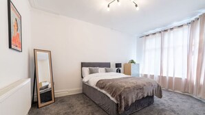 Un dormitorio con cama, cómoda, espejo y ventana con cortinas.