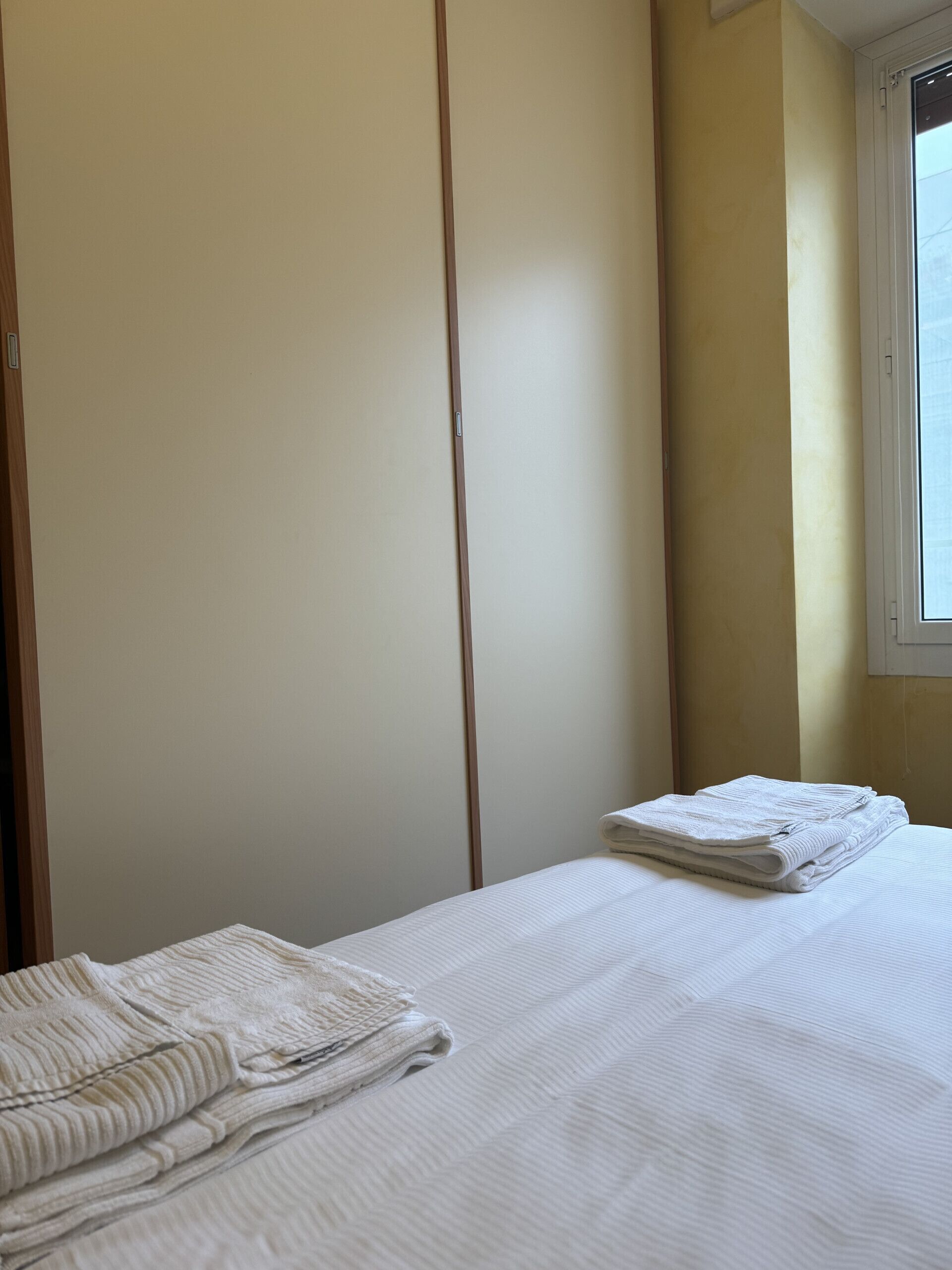 Een kamer met een bed, een raam en een kledingkast.