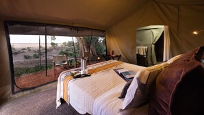 Ein Zeltraum mit Bett, Tisch mit Lampe und Blick auf die Wüste.