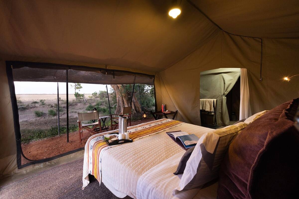A tented room with a bed, a table with a lamp, and a view of the desert.