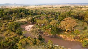 Ein Fluss schlängelt sich durch eine Savannenlandschaft mit vereinzelten Bäumen und einigen kleinen Gebäuden.