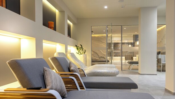 A modern spa area with reclining chairs, a massage table, and a glass-enclosed room with a stone wall.