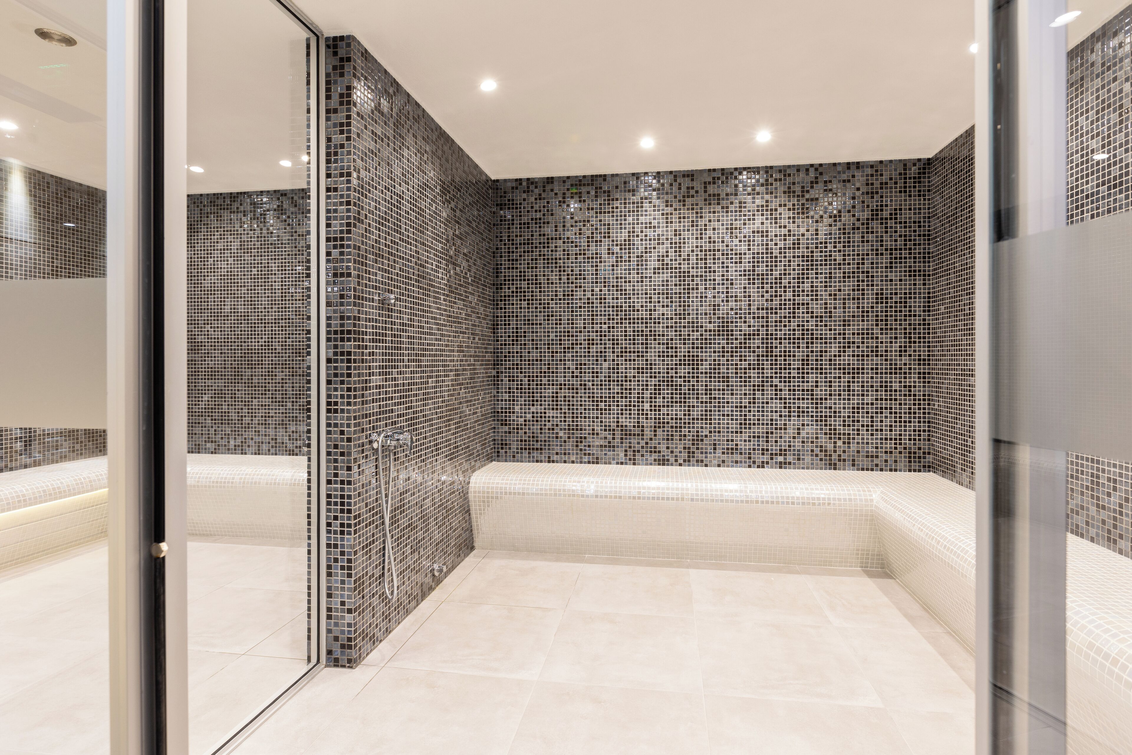 A modern bathroom with a glass partition, a tiled mosaic wall, and a white bathtub.
