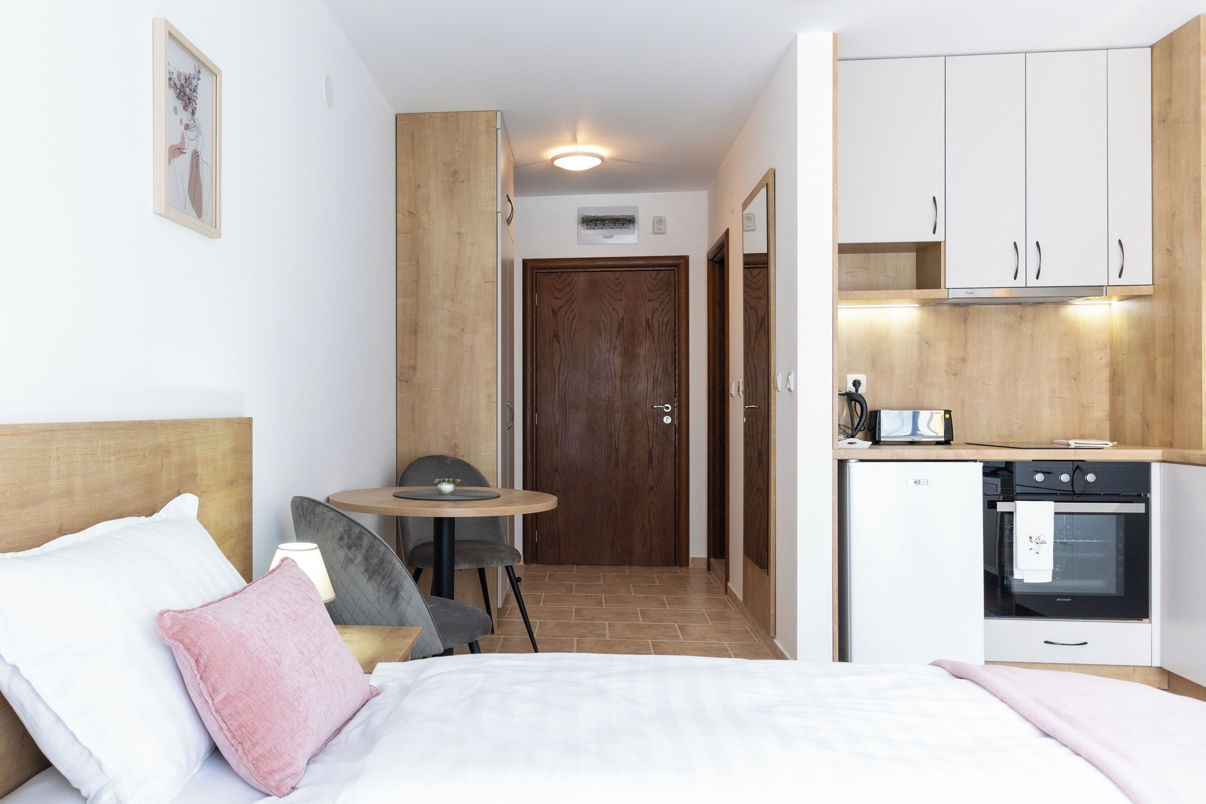 Une chambre d’hôtel de taille réduite, comprenant un lit, une table de chevet, une chaise, une petite table et une kitchenette.