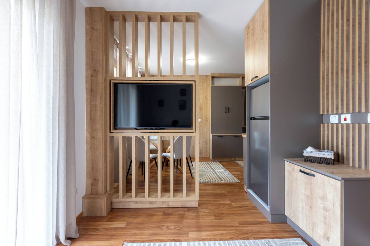 A modern kitchen with wooden cabinetry, a built-in TV, and a refrigerator.