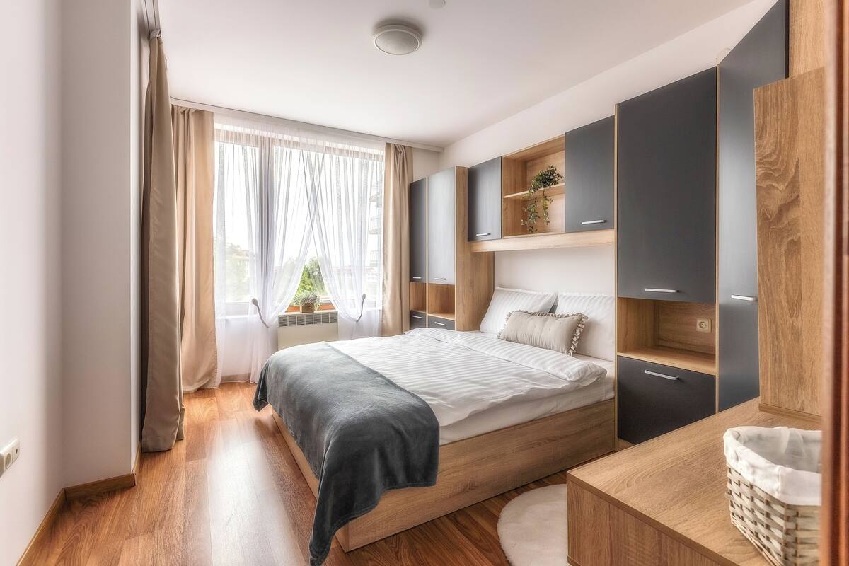 A modern bedroom with a wooden bed, built-in wardrobe, and a view of the outdoors.