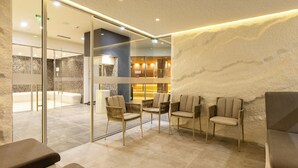 A modern waiting area with glass partitions, comfortable seating, and a visible relaxation area with a massage chair.