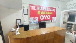 A reception desk with a wooden finish, a framed certificate on the wall, and a large promotional banner for The Jhunjhunu Palace AC & Non AC Rooms. - Oyo  The Jhunjhunu Palace Hotel (Jhunjhunu)