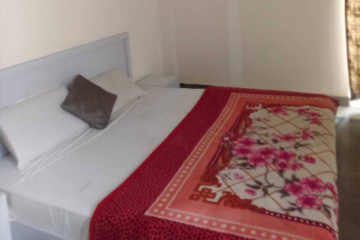 A bedroom with a bed, a pillow, and a red floral bedspread.