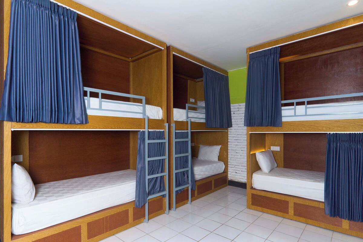 A room with four bunk beds, each with a mattress and pillow, and a ladder between the beds.