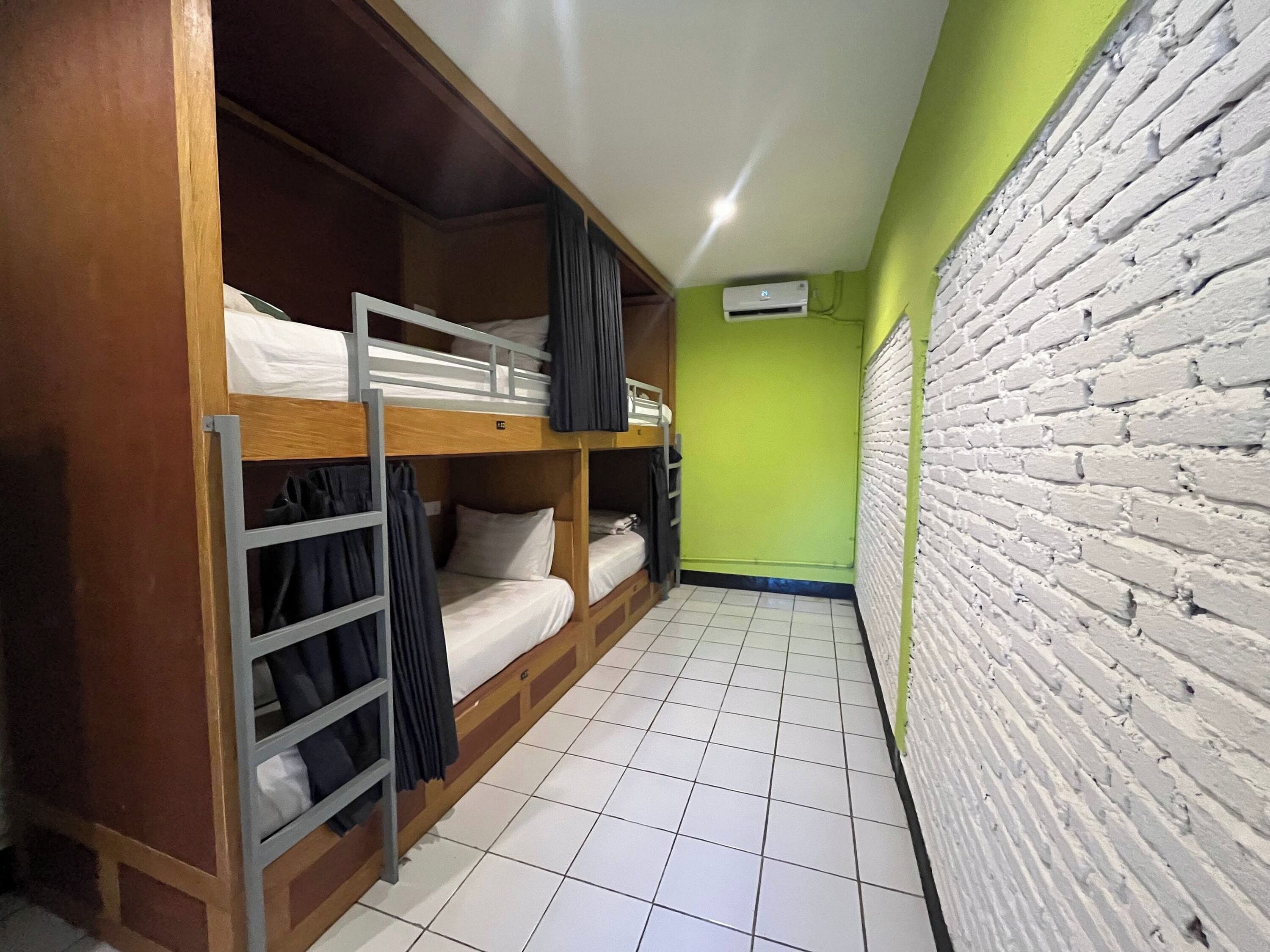 A dormitory room with bunk beds, a wardrobe, a tiled floor, and a brick wall.