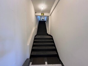 Una escalera estrecha y recta con barandilla, que conduce a una plataforma con una lámpara.