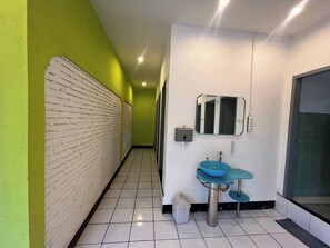 Un pasillo con pared de ladrillo blanco, un lavamanos azul y un espejo en la pared.